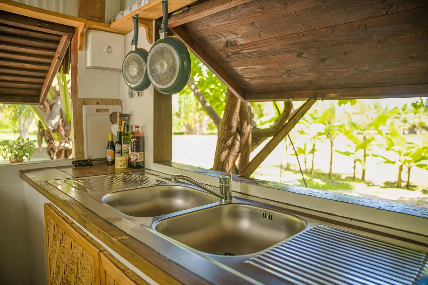 Détails charmants de la cuisine du Faré Totara, avec vue à travers la fenêtre sur la verdoyante végétation de Fare Tiaia Moorea, évoquant une connexion naturelle et sereine.