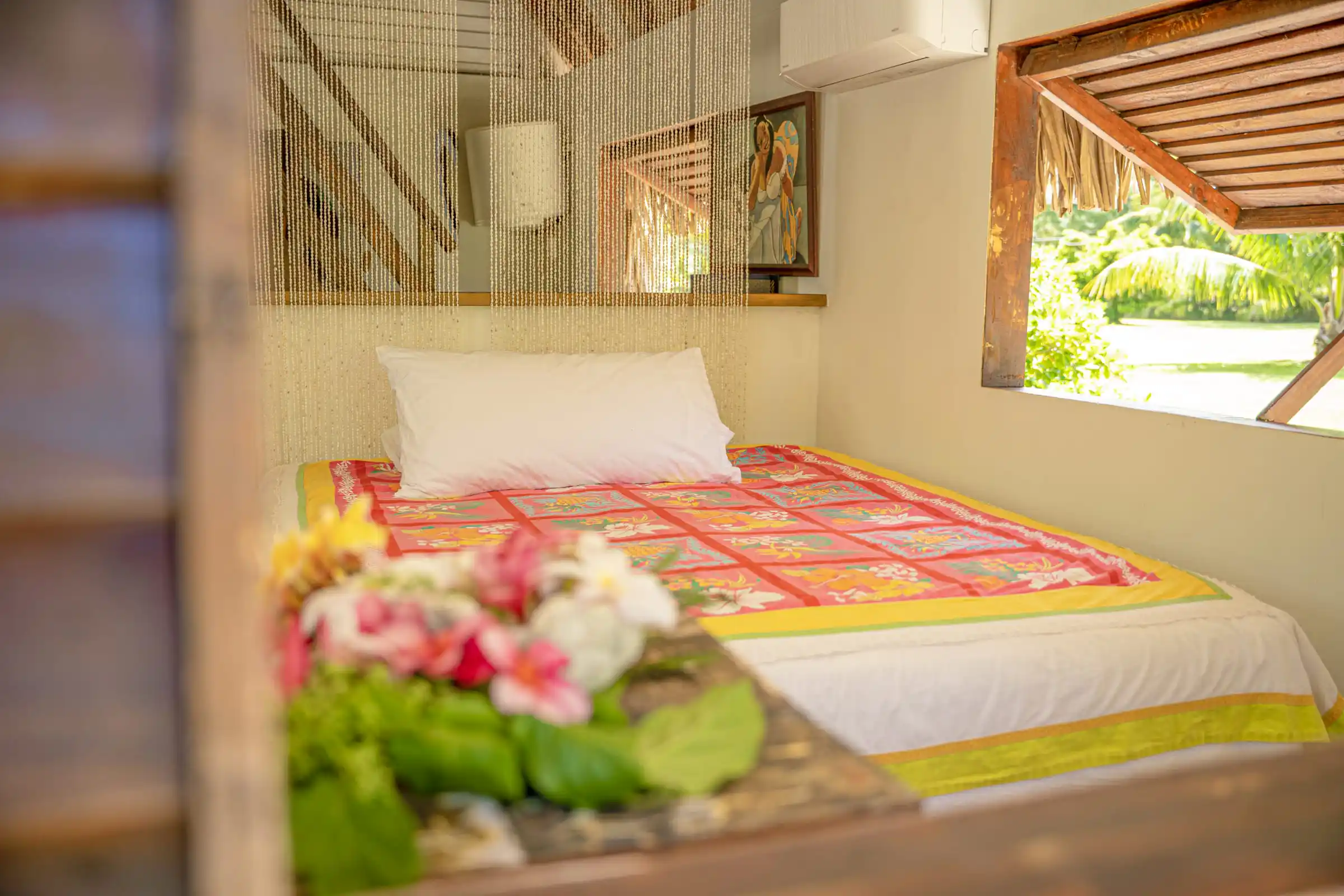 Vue intérieure de la chambre du Faré Totara à Fare Tiaia Moorea, agrémentée d'un rideau de coquillages captivant, avec une fenêtre ouverte sur la luxuriante végétation tropicale.