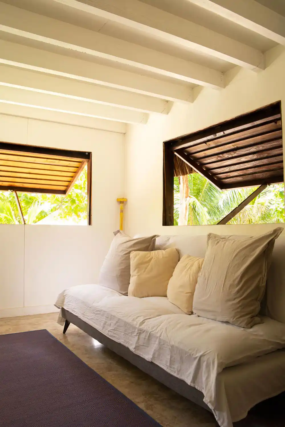 sCanapé-lit confortable dans le Faré Totara, près de la fenêtre offrant une vue apaisante sur la végétation luxuriante de Fare Tiaia Moorea.
